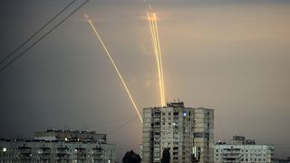 Two rockets cross the sky behind old apartment blocks.