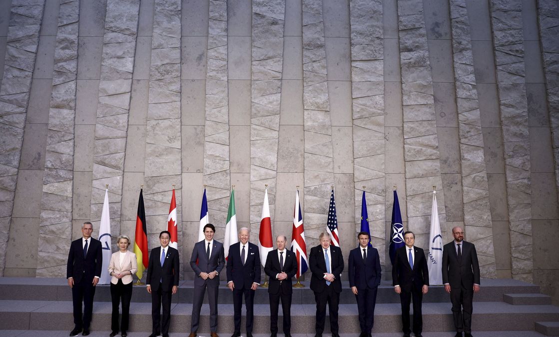 G7 summit participants pose in front of the flags of the G7, Germany, Canada, France, Italy, Japan, the UK, the US, the EU and NATO. 
