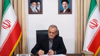 Der Präsident Irans am Schreibtisch vor zwei iranischen Flaggen