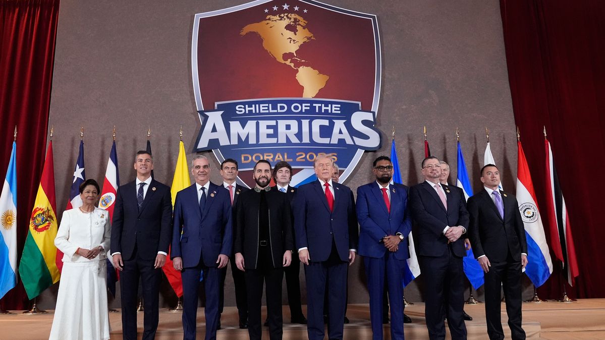 US-Präsident Donald Trump (Mitte) posiert mit den Teilnehmern des Gipfeltreffens „Shield of the Americas“ für ein Gruppenfoto. Politiker und eine Politikerin stehen vor Flaggen und einem Logo des Shield of the Americas.