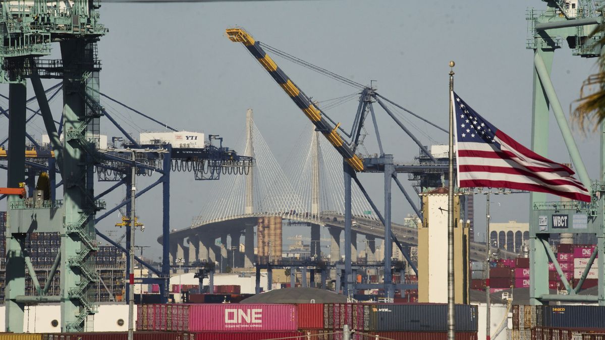 Eine US-Flagge weht vor Schiffscontainern und einer großen Brücke
