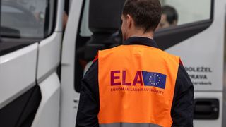 Ein Mann mit einer orangen Warnweste mit dem ELA Logo steht vor einem LKW.