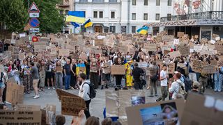 Eine Menschenansammlung mit Protestschildern und Ukraineflaggen.