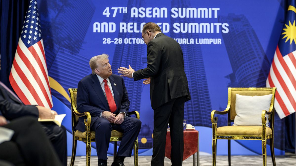 US-Präsident Donald Trump sitzt, umgeben von zwei Flaggen, Malaysias Premierminister Anwar Ibrahim steht vor ihm