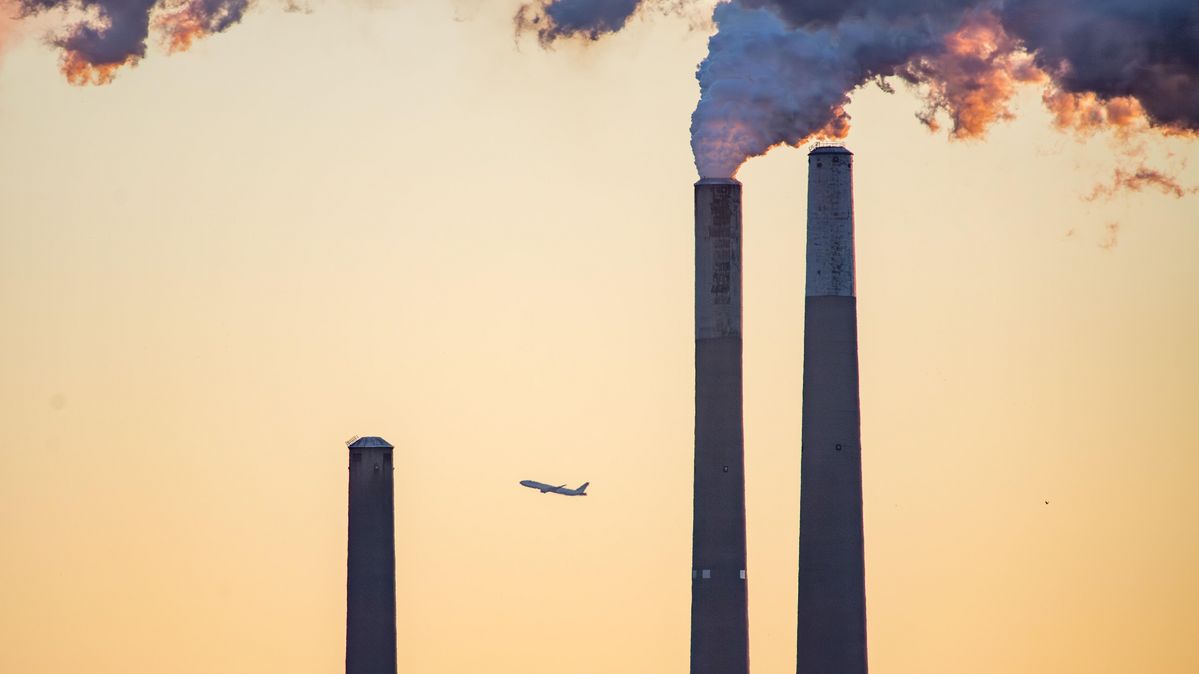 An airplane passes the steam from the chimneys of a power station.