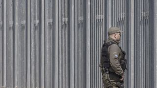 Ein Polizist in Uniform vor einem hohen Grenzzaun