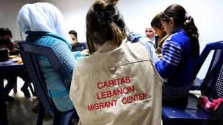 Eine Person, die eine Jacke mit der Aufschrift »Caritas Lebanon Migrant Center« trägt, leitet eine Gruppe von Kindern an.