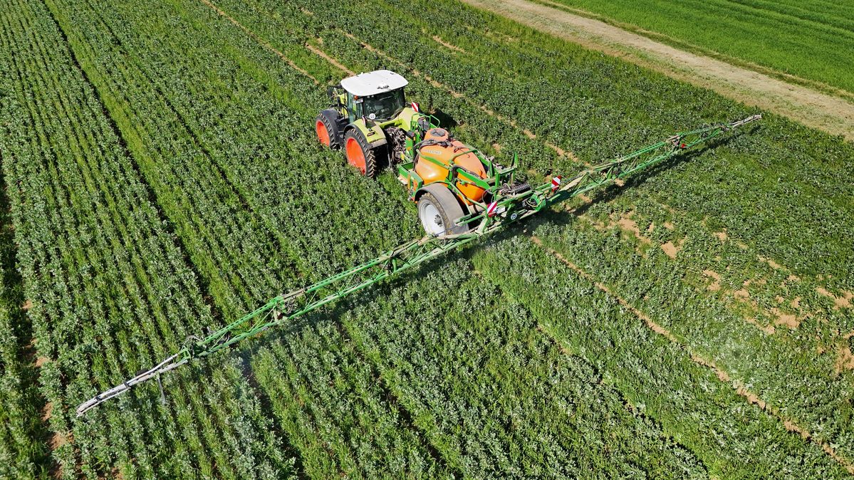 Ein Traktor fährt über ein grünes Feld mit einer Spritzmaschine.