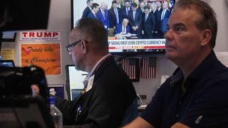 Zwei Männer vor einem Fernseher, in dem Präsident Trump ein Dokument unterschreibt