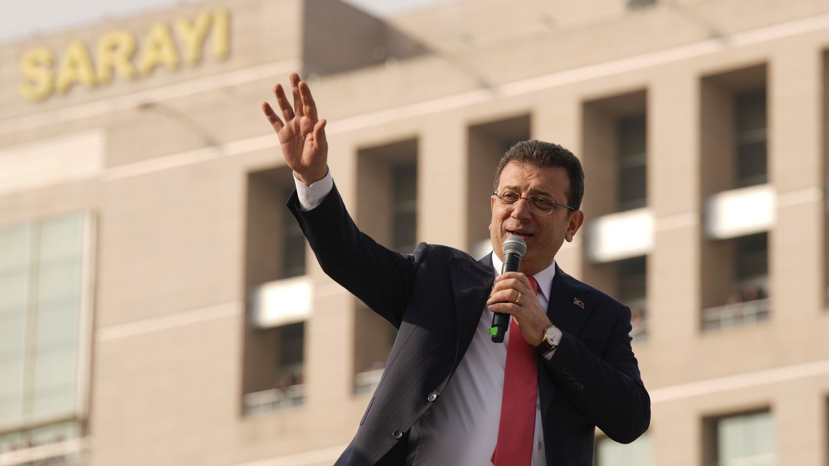 Ekrem İmamoğlu mit erhobener Hand und Mikrophon vor dem Gerichtsgebäude in Istanbul.